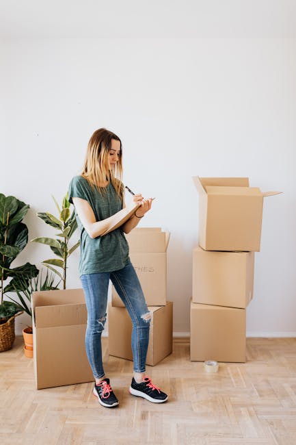 Two professional movers from Man with Van Lisson Grove are engaged in the loading process of a home relocation, carrying a large, heavy, green upholstered piece of furniture into the back of a white cargo van parked on a paved street. The van's rear doors are wide open, revealing the spacious interior designed for furniture transport, with a visible black protective mat on the floor. One mover, dressed in dark clothing and wearing protective eyewear, is pulling the furniture towards the vehicle, while the other, in a navy blue jacket and red sneakers, is supporting the furniture from the opposite side. The surrounding environment includes a street sign on a pole, casting natural daylight onto the scene, and a curb with a concrete sidewalk, facilitating efficient packing and loading for furniture removal services. This image illustrates the careful handling and structured loading process typical of professional removals operations, emphasizing the importance of proper packing and transport logistics for home relocations, as offered by Man with Van Lisson Grove.